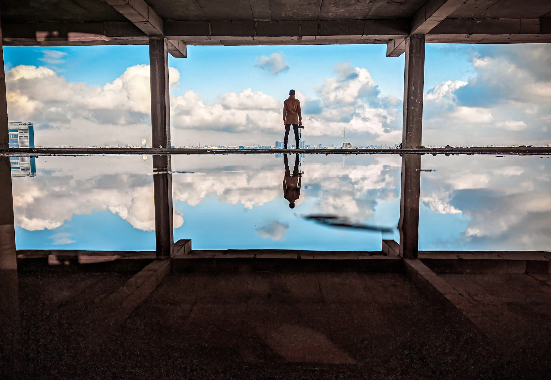 Persona de pie frente a un gran ventanal que refleja el cielo